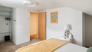 Habitación de hotel con cama, mesita de noche con lámpara, un cuadro en la pared y una puerta que da a otra habitación.
