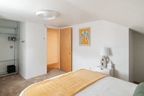 Una camera d'albergo con un letto, un comodino con una lampada, un quadro appeso al muro e una porta che dà su un'altra stanza.