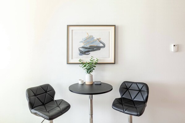Une pièce comprenant deux fauteuils en cuir noir, une petite table ronde avec un vase blanc et une plante, et un tableau abstrait encadré accroché au mur.