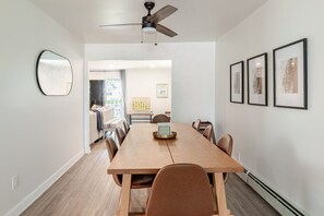 Un coin repas avec une table en bois, des chaises, un ventilateur de plafond et des œuvres d’art encadrées accrochées aux murs.