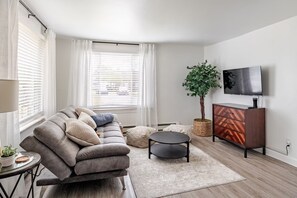 A modern living room with a sofa, ottoman, TV, and a plant.