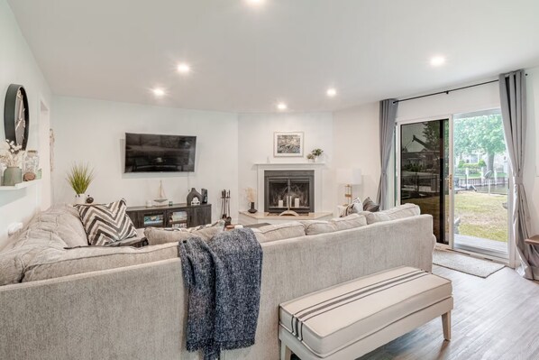 A modern living room with a sofa, a bench, a fireplace, and a large window with curtains.