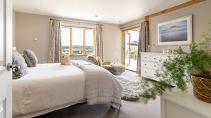 Une chambre à coucher avec un grand lit, une commode, une fenêtre donnant sur la campagne et un tableau accroché au mur.