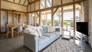 Un salon spacieux avec un grand canapé, une table à manger avec des chaises et un téléviseur. La pièce est dotée de grandes fenêtres qui offrent une vue sur la campagne.