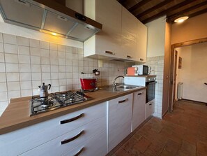 Una cucina con un fornello a gas, un bollitore rosso, un forno a microonde e un lavello.