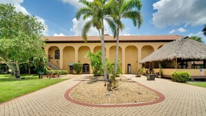 A courtyard with a tiled floor, palm trees, and a building with arches and a thatched roof. - POI Resort Studio Near Everglades NP: Swim + Sail (Naples)