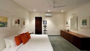 Ein Hotelzimmer mit einem großen Bett, einem Deckenventilator, einer Klimaanlage, einem hölzernen Schminktisch und gerahmten Bildern an den Wänden.