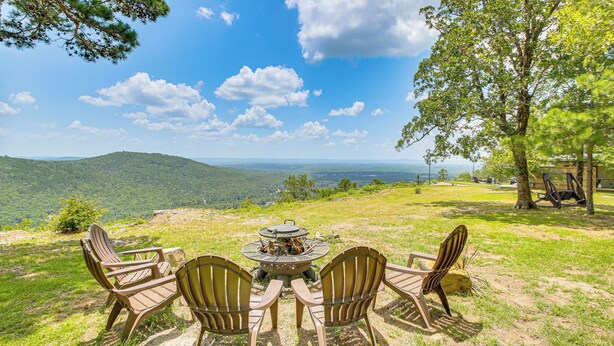 Un espacio al aire libre con vistas panorámicas a un paisaje montañoso, con sillas tipo Adirondack y una chimenea.