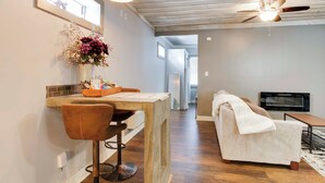 Una cocina moderna con techo de madera, zona de comedor con taburete de bar, sofá y televisor.