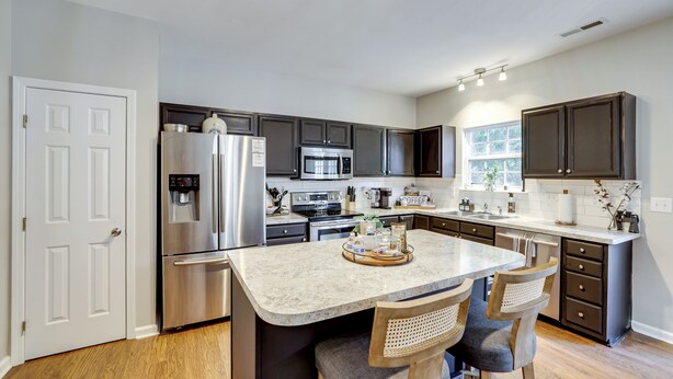 A modern kitchen with dark cabinets, stainless steel appliances, and a central island with bar stools. - Playroom & Home Office: Family Retreat in Mauldin! (Mauldin)