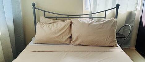 A bed with a metal frame and two pillows, a chair, and a window with curtains.