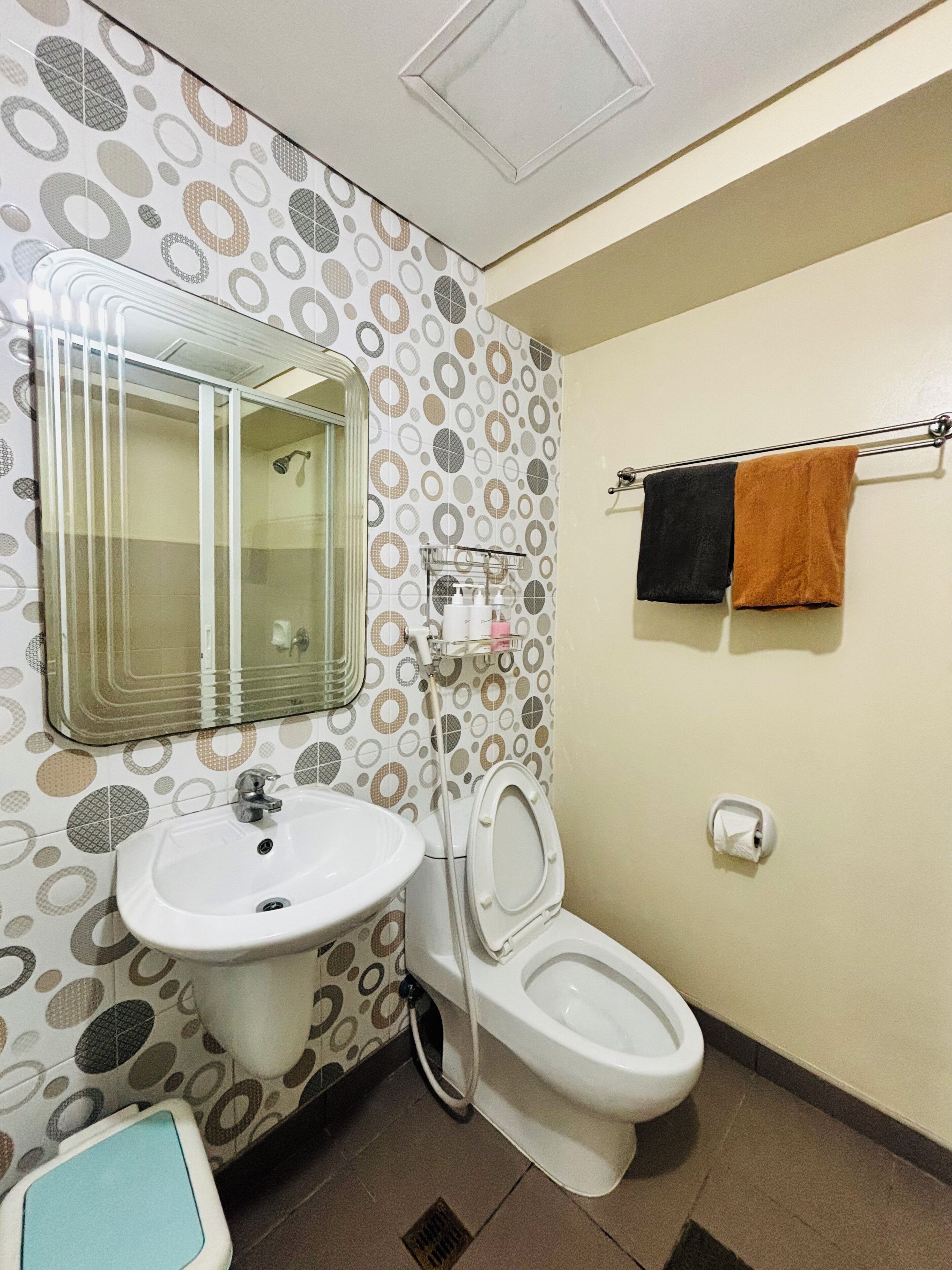 A bathroom with a toilet, sink, and mirror. There are towels hanging on a rack.