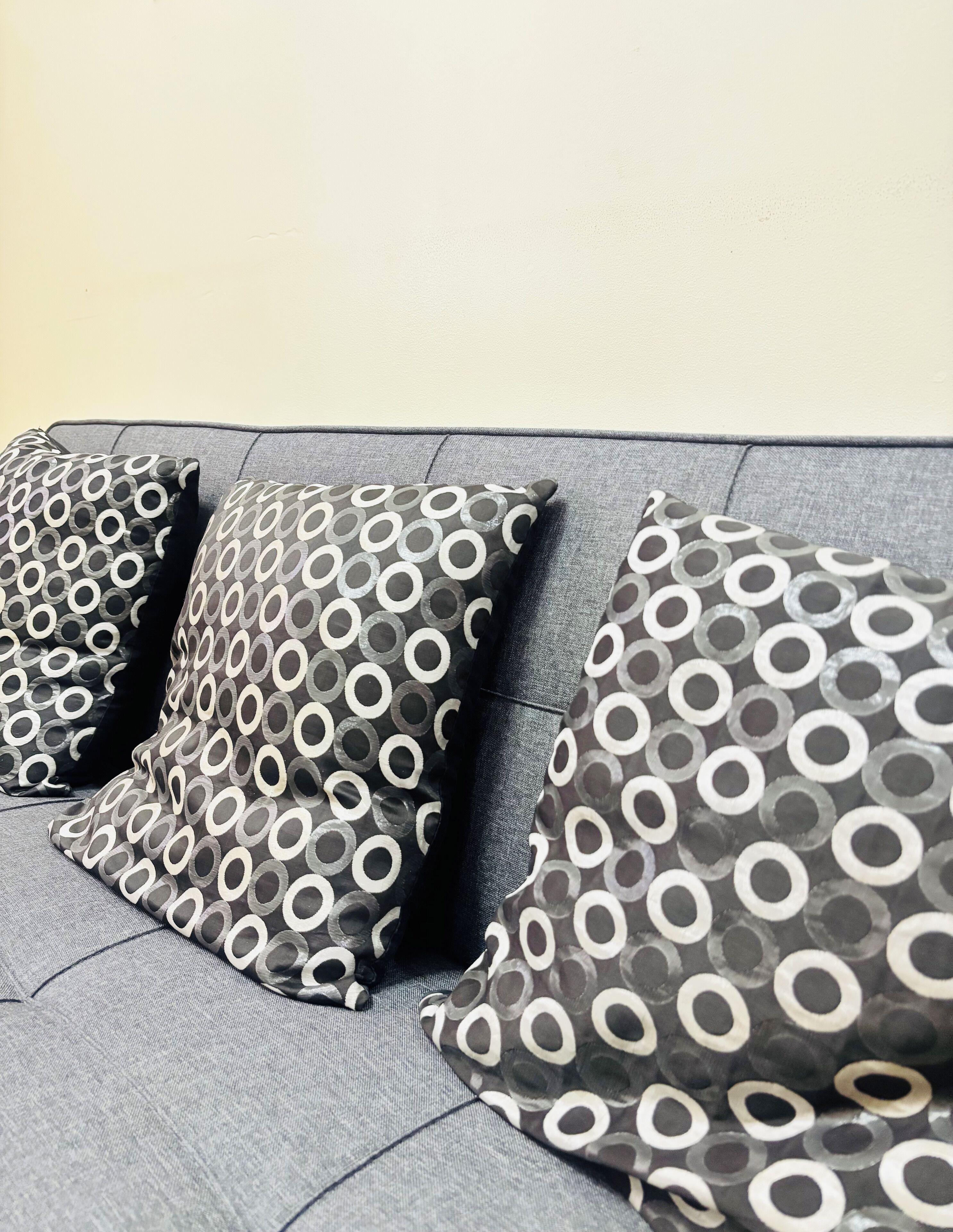 A grey sofa with three circular patterned cushions.