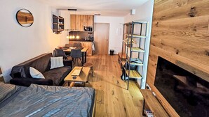 Ein kompakter Wohnraum mit Küchenzeile, Essbereich, Sofa, Bett und einer eingebauten Bücherreol.