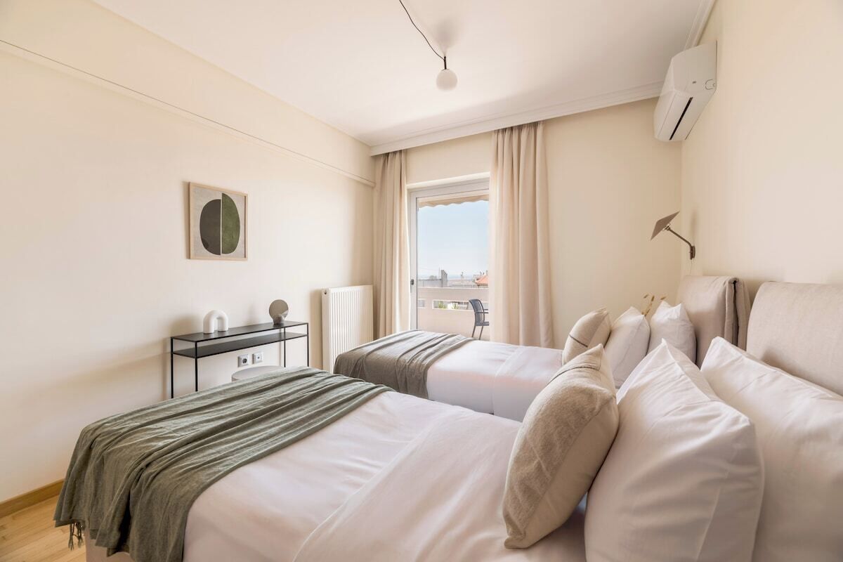 A hotel room with two beds, a desk, a chair, and a window with curtains.