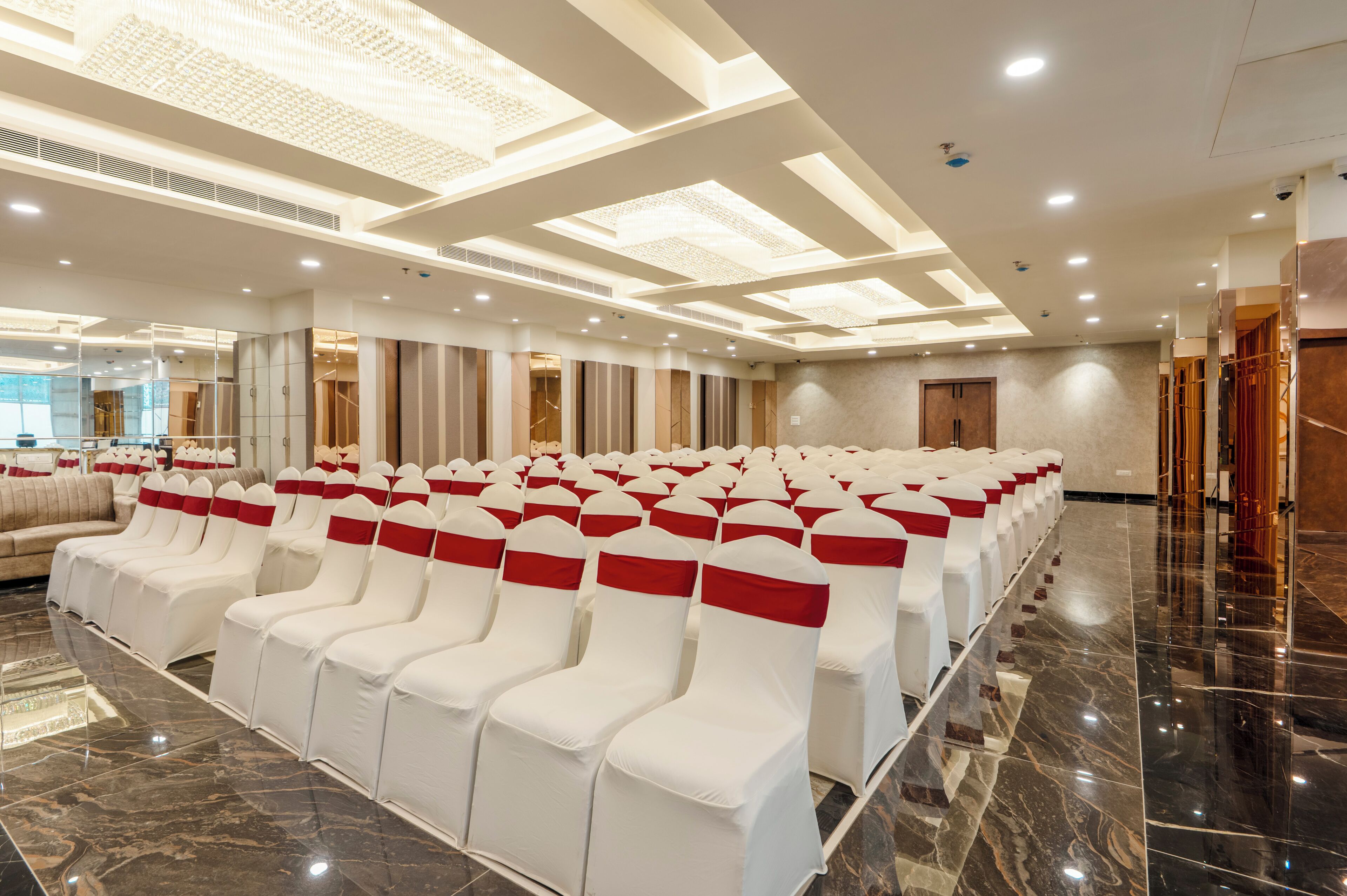A hotel conference room with rows of white chairs with red sashes, a polished marble floor, and a modern ceiling design with recessed lighting.