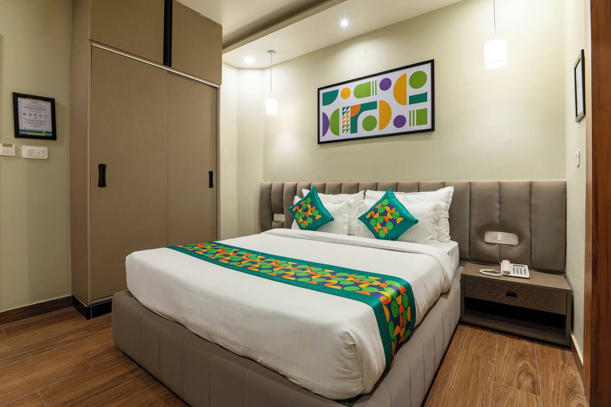 A hotel room with a bed, a nightstand, a phone, and a wall-mounted artwork.