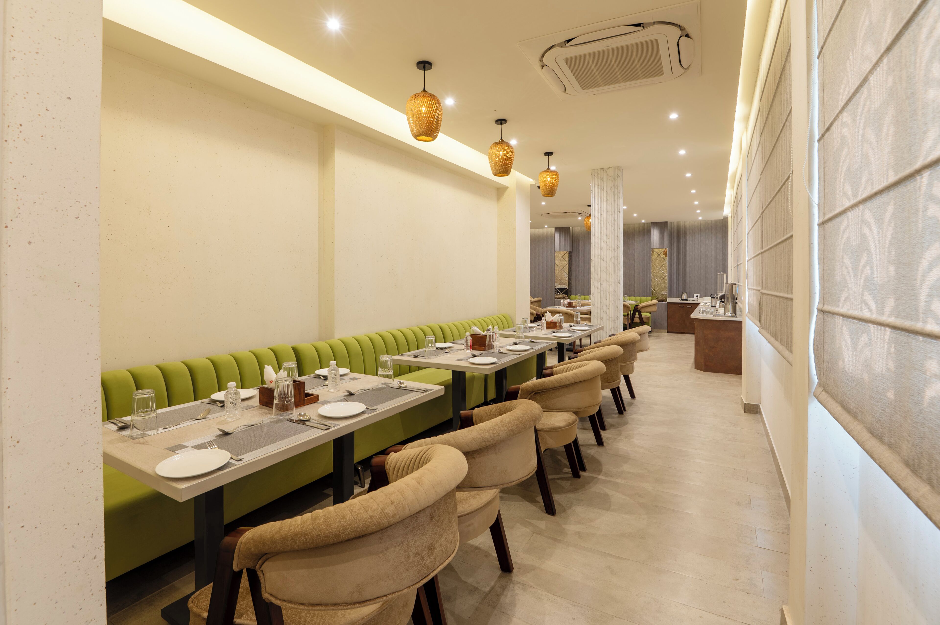 Un ristorante con sedute verdi, sedie beige e un lungo tavolo con piatti e bicchieri.