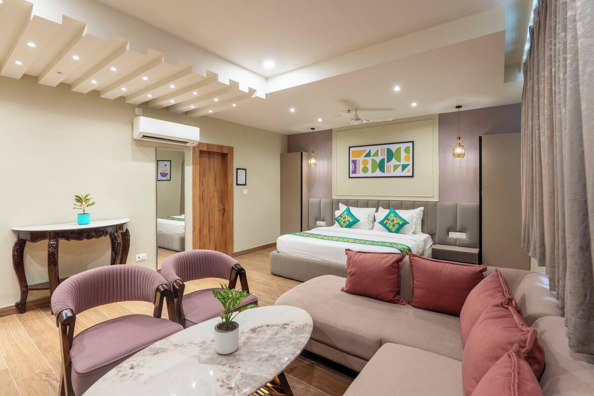 A modern hotel room with a bed, sofa, chairs, a small table, and a ceiling light fixture.