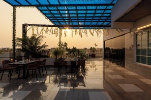 A rooftop terrace with a glass ceiling, dining table, chairs, and potted plants. - Treebo Premium Gateway Triveni (Prayagraj)