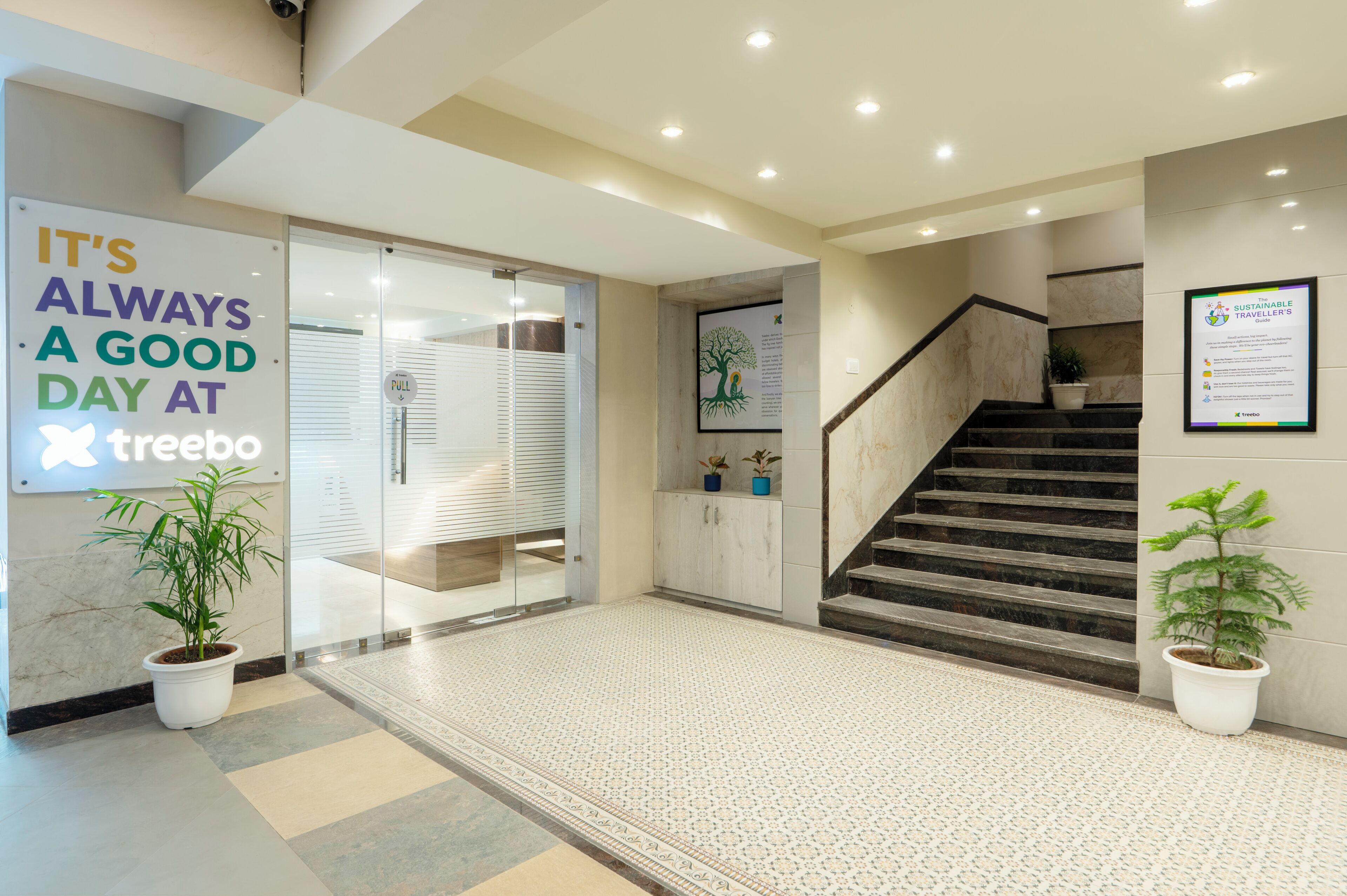 A modern hotel lobby with a glass door entrance, a staircase, and a sign promoting sustainable travel.