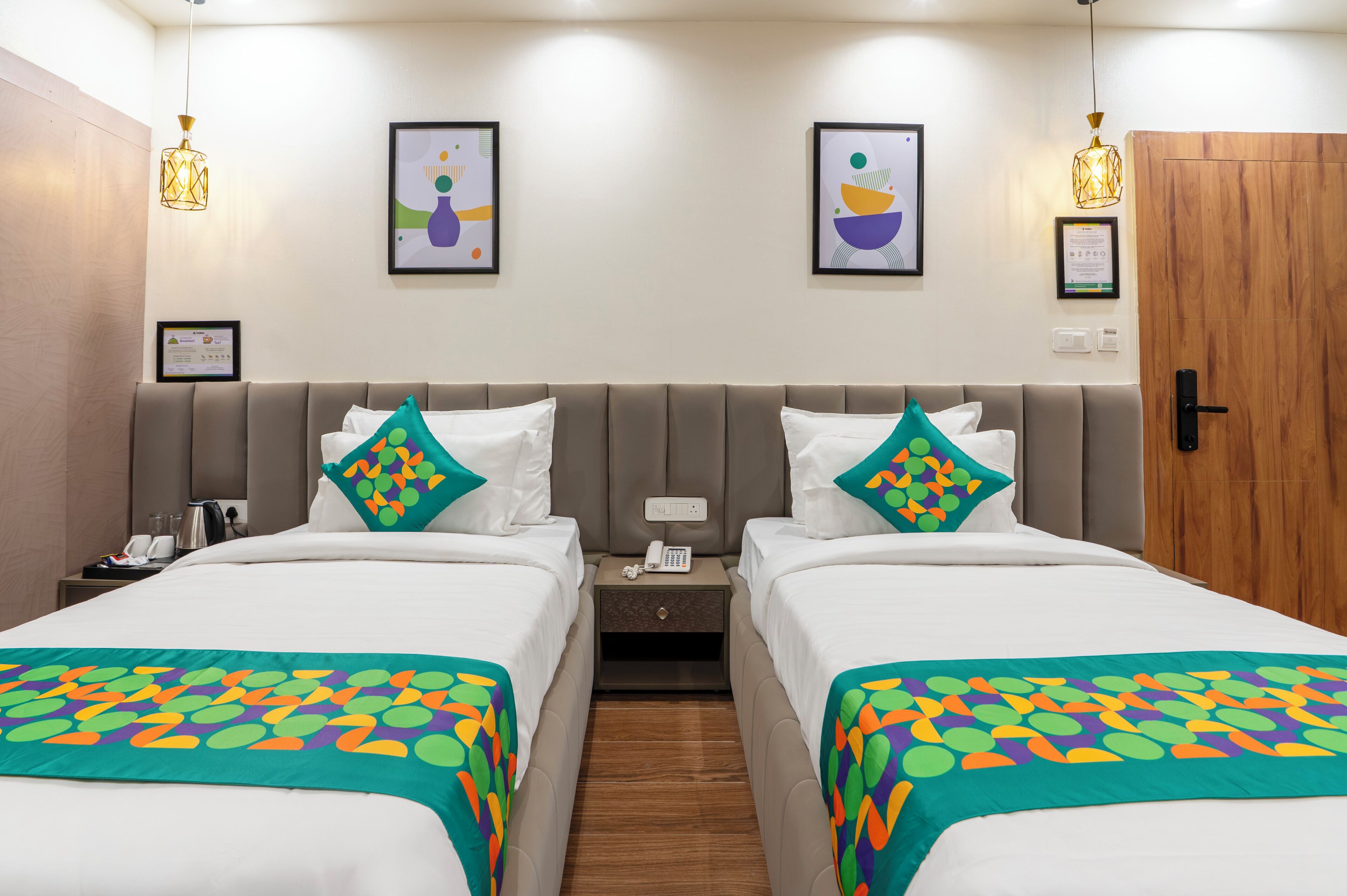 A hotel room with two beds, a wooden door, and artwork on the walls.