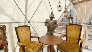 Una habitación con toldo, dos sillas doradas, una mesa y una estatua de un caballero.