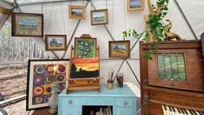 Una tienda de campaña con obras de arte en las paredes, un piano y un escritorio con cajones.