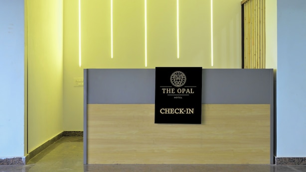 A reception desk with a sign reading "The Opal Hotel Check-in" and vertical light strips on the wall. - The Opal Hotel (Greater Noida)