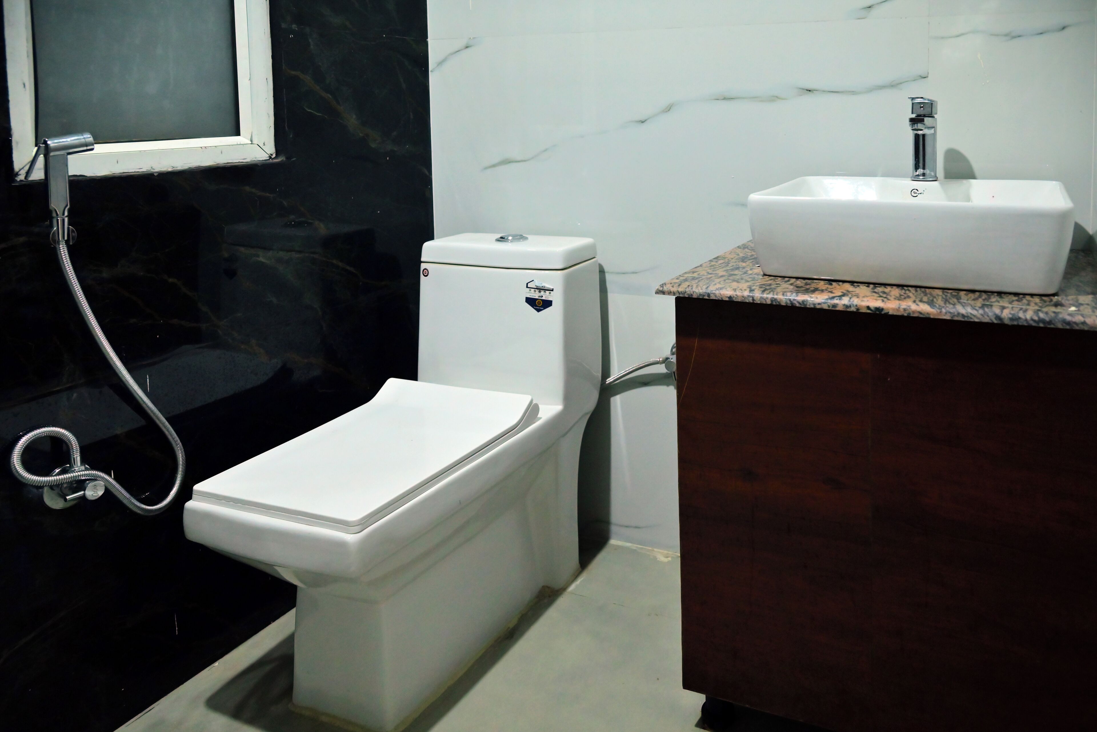 A bathroom with a white toilet, a sink with a marble countertop, and a shower with a black wall.