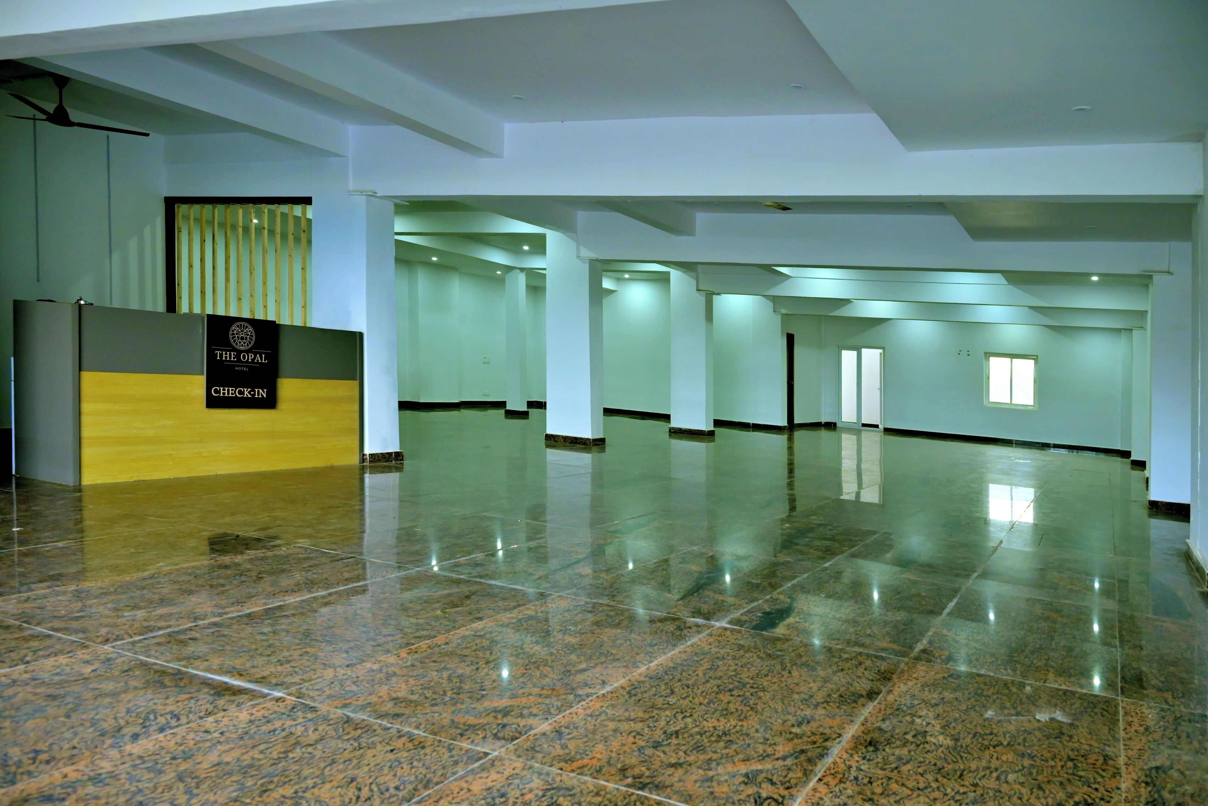 A spacious hotel lobby with a check-in counter, a ceiling fan, and a polished marble floor.