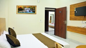 A hotel room with a bed, pillows, a painting, a wooden door, a TV, and a desk. - The Opal Hotel (Greater Noida)