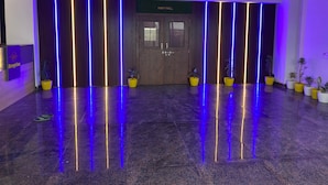 A reception area with a reception desk, a party hall sign, and potted plants. - The Opal Hotel (Greater Noida)