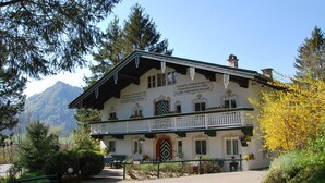 A traditional Alpine-style building with a balcony, surrounded by greenery and mountains.