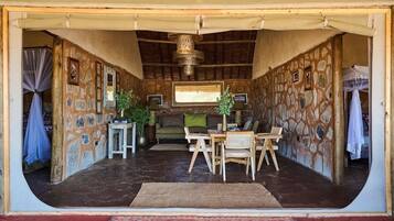 An open-plan living area with a stone wall, a sofa, a dining table with chairs, and a large window.