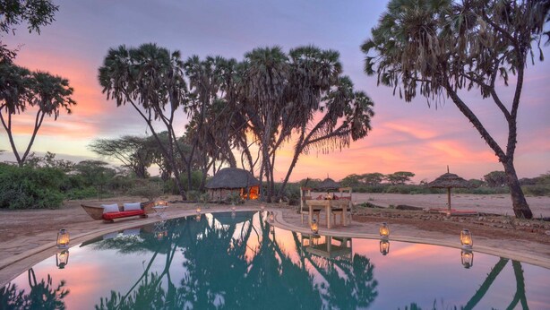 A serene outdoor pool area with a thatched-roof hut, surrounded by tall trees and a sunset sky. - Saruni Rhino (Kauro)