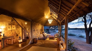 A cozy interior with a stone wall, wooden furniture, and a view of the outdoors. - Saruni Rhino (Kauro)