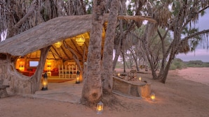 A rustic thatched-roof structure with a cozy interior, surrounded by trees and a sandy landscape. - Saruni Rhino (Kauro)