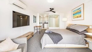 Une chambre d’hôtel moderne équipée d’un lit, d’un bureau, d’une chaise, d’une télévision, d’un climatiseur, d’un ventilateur de plafond et d’une salle de bain avec une paroi en verre.
