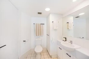 A modern bathroom with a toilet, sink, and mirror. - Wake to the Waves - Oceanfront Apartment (Fraser Coast)