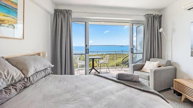 Une chambre avec un grand lit, une chaise, une petite table et un balcon donnant sur la mer.