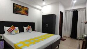 A hotel room with a bed, a wardrobe, a painting on the wall, and a window with curtains. - Coco TreeHotel (Gurugram)