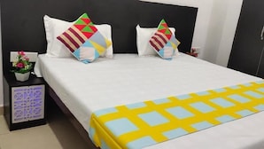 A double bed with a white and yellow bedspread, two pillows with geometric patterns, a nightstand with a decorative item, and a wall with a geometric light fixture. - Coco TreeHotel (Gurugram)