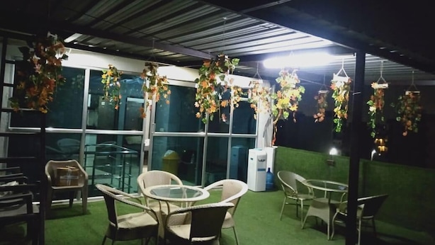 An indoor patio area with hanging floral arrangements, seating, and a view of the outside through large windows. - Coco TreeHotel (Gurugram)