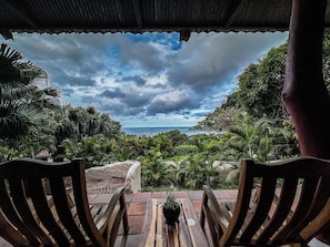 A wooden bench with a potted plant, overlooking a lush landscape with a view of the sea under a cloudy sky.