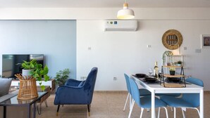 A modern living room with a TV, blue chairs, a dining table, and a hanging light fixture. - Chloris 3- Bedroom Apartment in Larnaca (Larnaca)