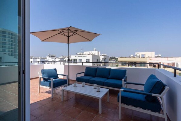 A balcony with a sofa set, a table, and an umbrella. - Chloris 3- Bedroom Apartment in Larnaca (Larnaca)