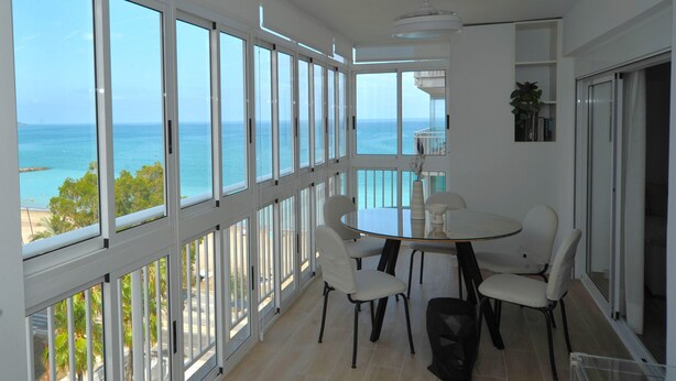 A balcony with a view of the sea, a round table with chairs, and a ceiling fan. - ESTORIL VISTAMAR PREMIUM SPECIAL (Benicàssim)