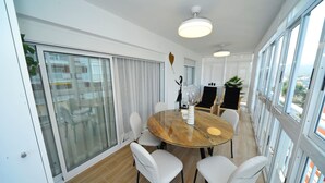 A modern dining area with a round table, white chairs, and a large window with a view of buildings. - ESTORIL VISTAMAR PREMIUM SPECIAL (Benicàssim)