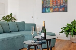 Une pièce avec un canapé de couleur turquoise, une petite table ronde sur laquelle sont posés deux verres et une bouteille de champagne, et un tableau accroché au mur.